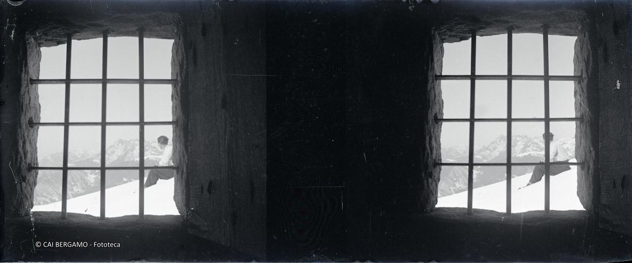 Skiatore seduto, visto dalla finestra con grata della baita