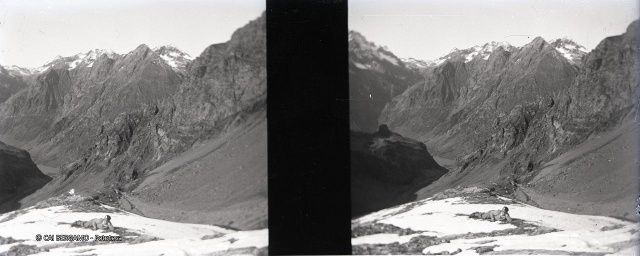 Disteso nell'erba tra macchie di neve col lago del Barbellino sullo sfondo