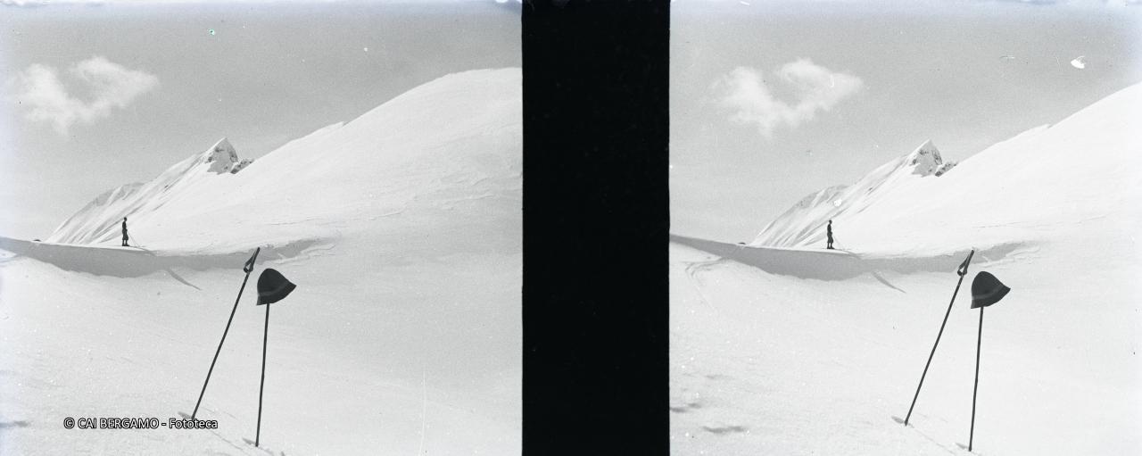 Scialpinista sullo sfondo e cappello su bastoncino in primo piano