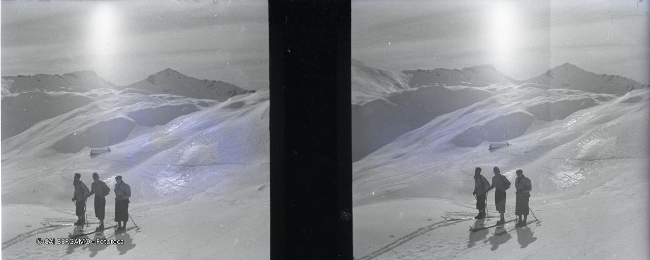 Tre scialpinisti con un gran sole alle spalle, in un vasto panorama innevato