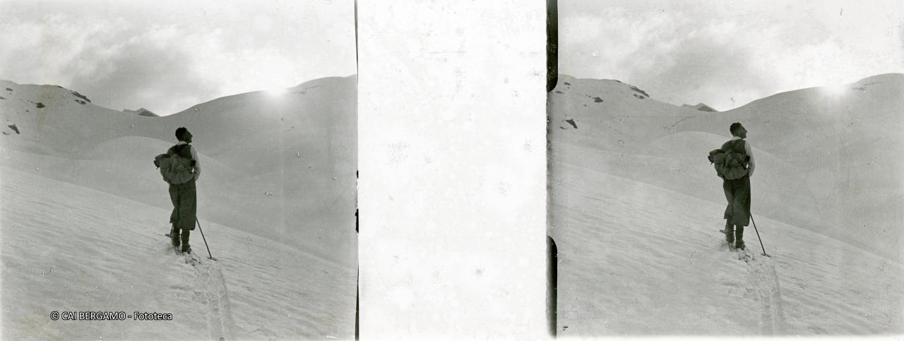 Scialpinista in contemplazione e con sole che spunta dal profilo innevato