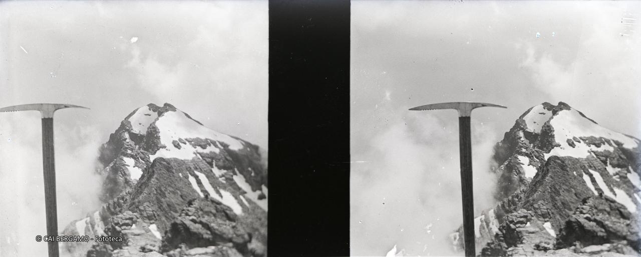 Piccozza in primo piano con retrostante cima rocciosa