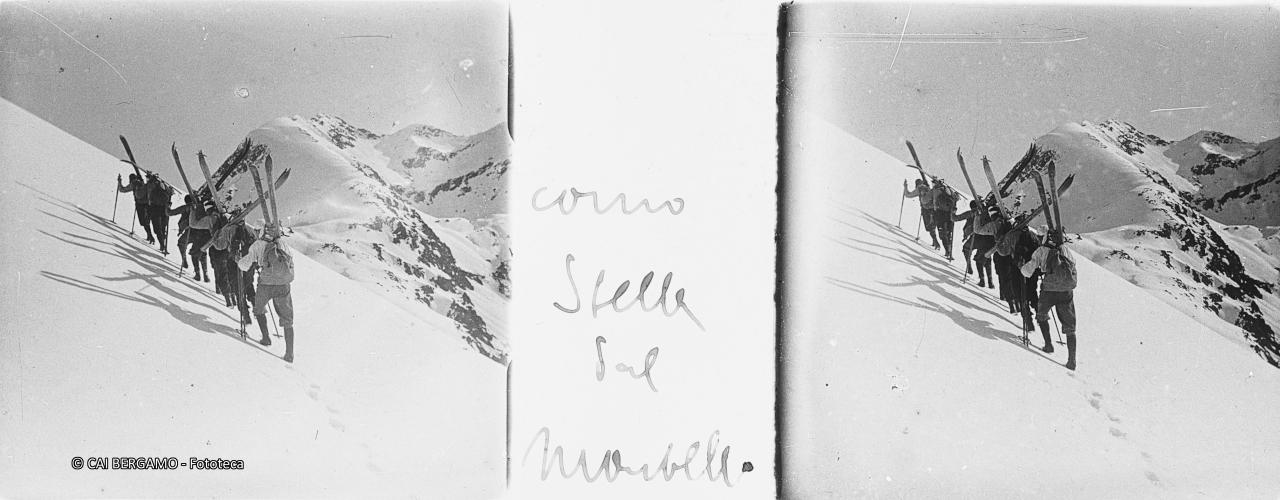 In salita sul Montebello con gli sci a spalla ed il Corno Stella sullo sfondo