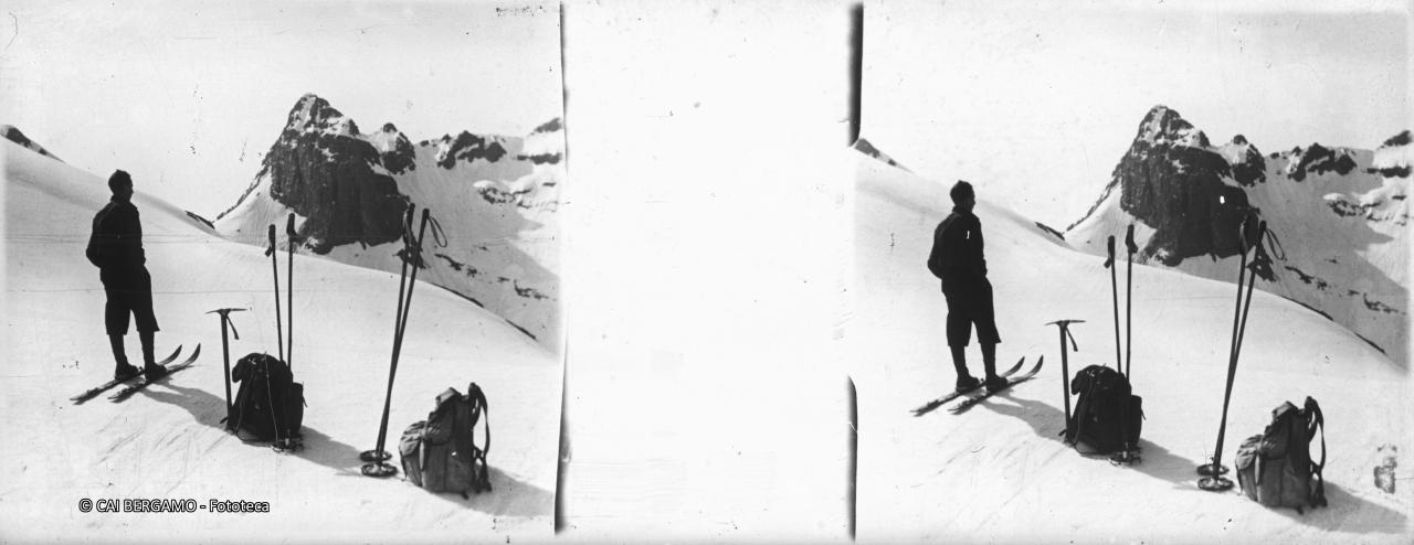 Sciatore tra bastoncini e zaini dei compagni di gita sotto lo sguardo del Poris con il passo di Valsecca