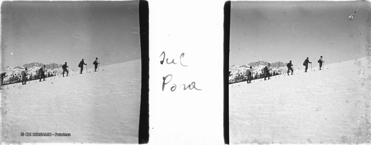 Sciatori in fila indiana verso cima Pora sotto lo sguardo della Presolana