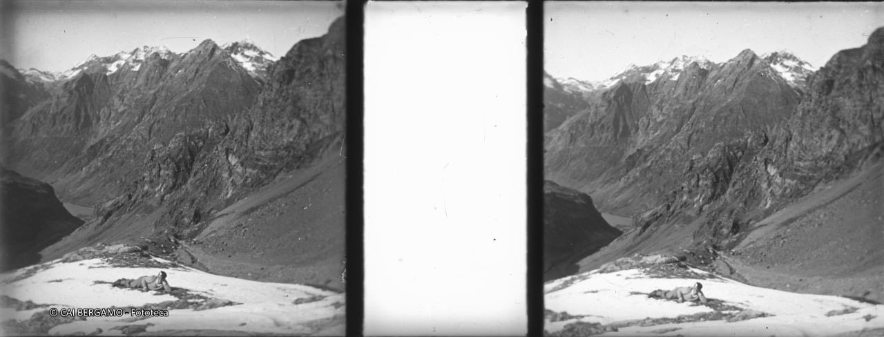 Sdraiato tra chiazze di neve in Val Cerviera con il Cavrel e Cappuccello alle spalle, con lo scorcio sul lago del Barbellino a valle