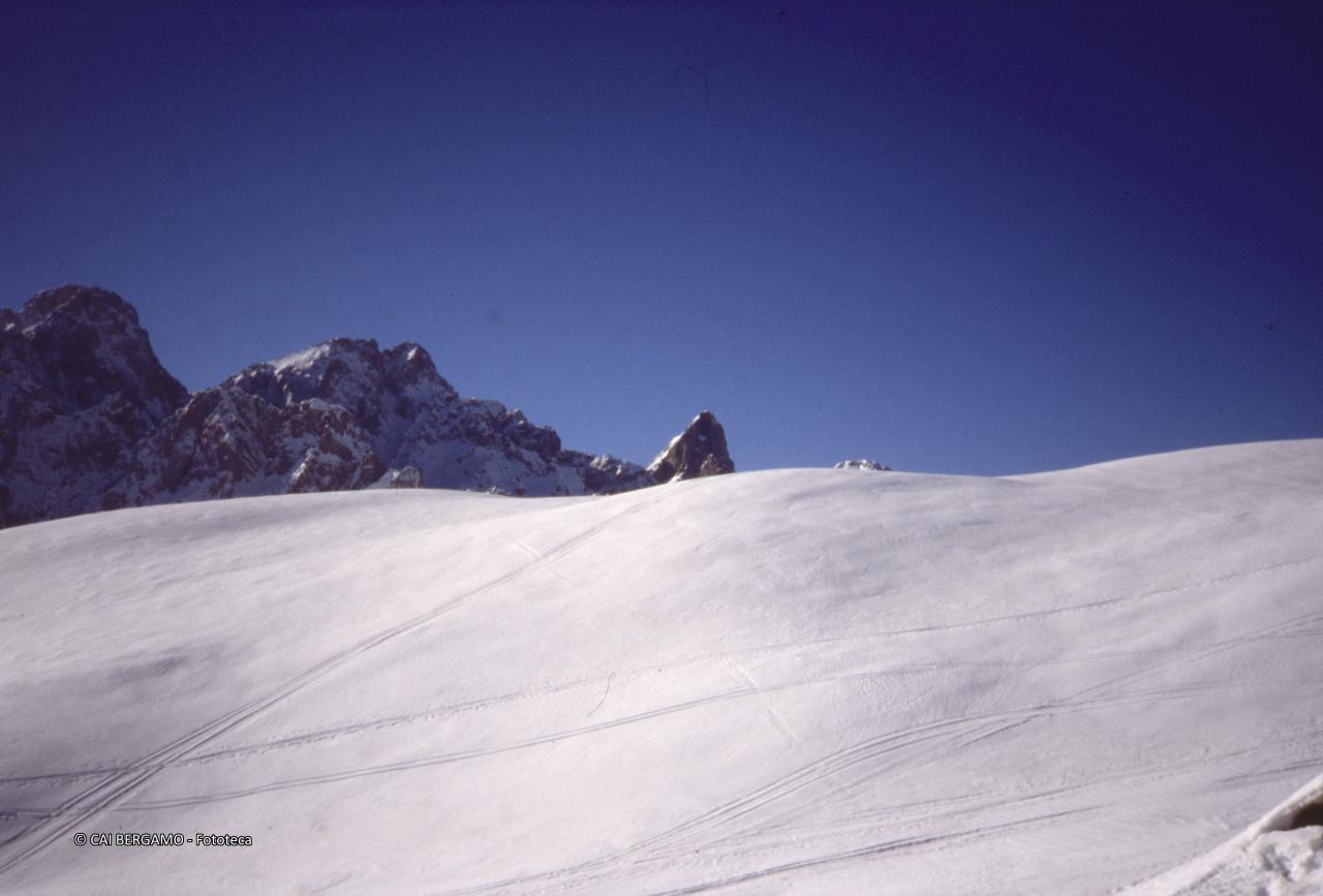 Dal profilo innevato del passo Campelli, spuntano da destra:  Cima Mengol, cima delle Casse Larghe e Cimon della Bagozza