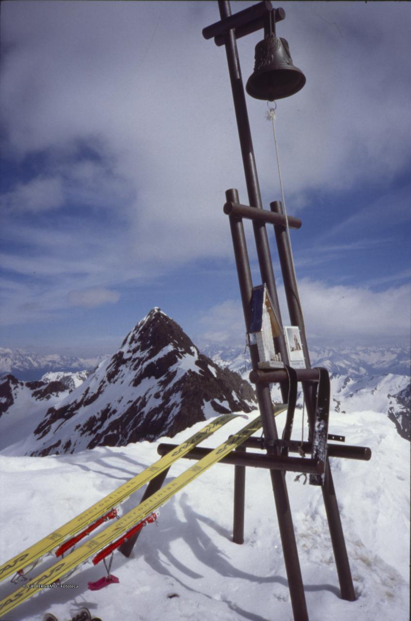 La campanella in vetta al Pizzo con sci a "riposo" ed il Monte Gleno sullo sfondo