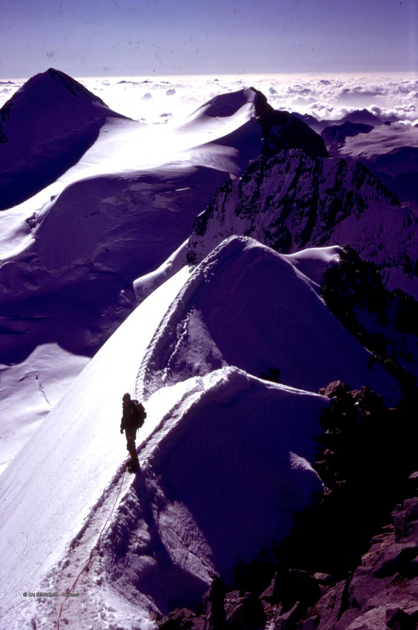 Zupò sulla sx e Argient sulla ds,  con primo piano su alpinista lungo traccia innevata sulla cresta